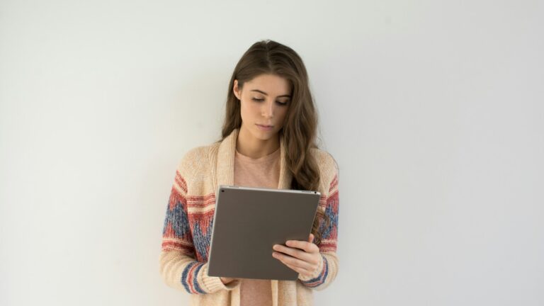 woman in beige, gray, and red sweater holding silver tablet computer