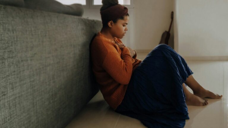 man in orange long sleeve shirt sitting on gray couch