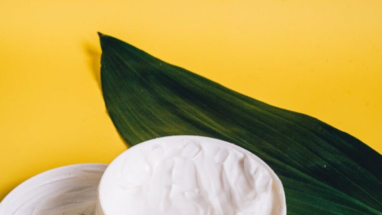 Open cosmetic cream container with a green leaf on a vibrant yellow backdrop, showcasing natural beauty.